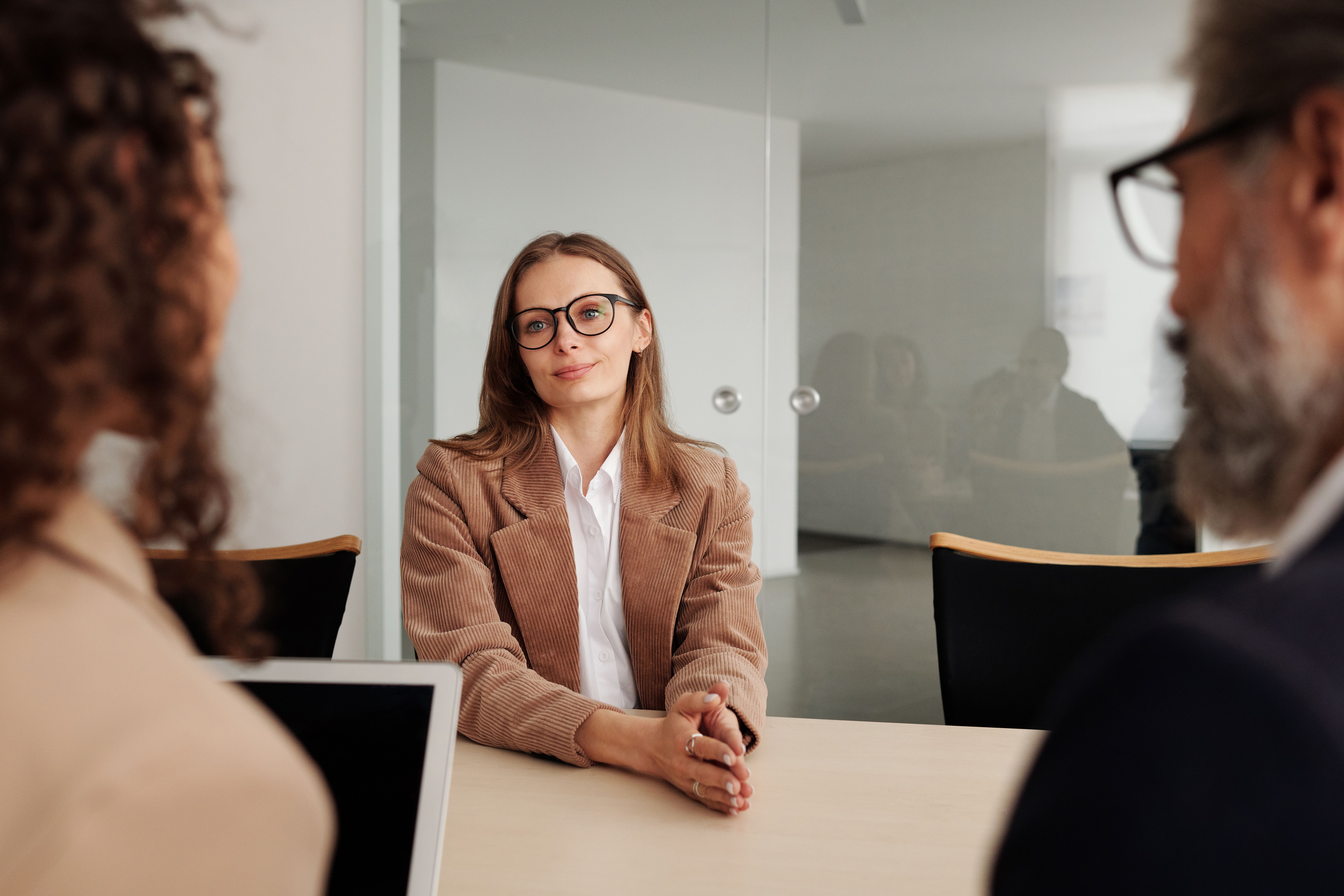 Fachkraft mit Brille sitzt im Vorstellungsgespräch zwei Gesprächspartner:innen gegenüber und hört aufmerksam zu, Symbol für Gedanken, die unausgesprochen bleiben