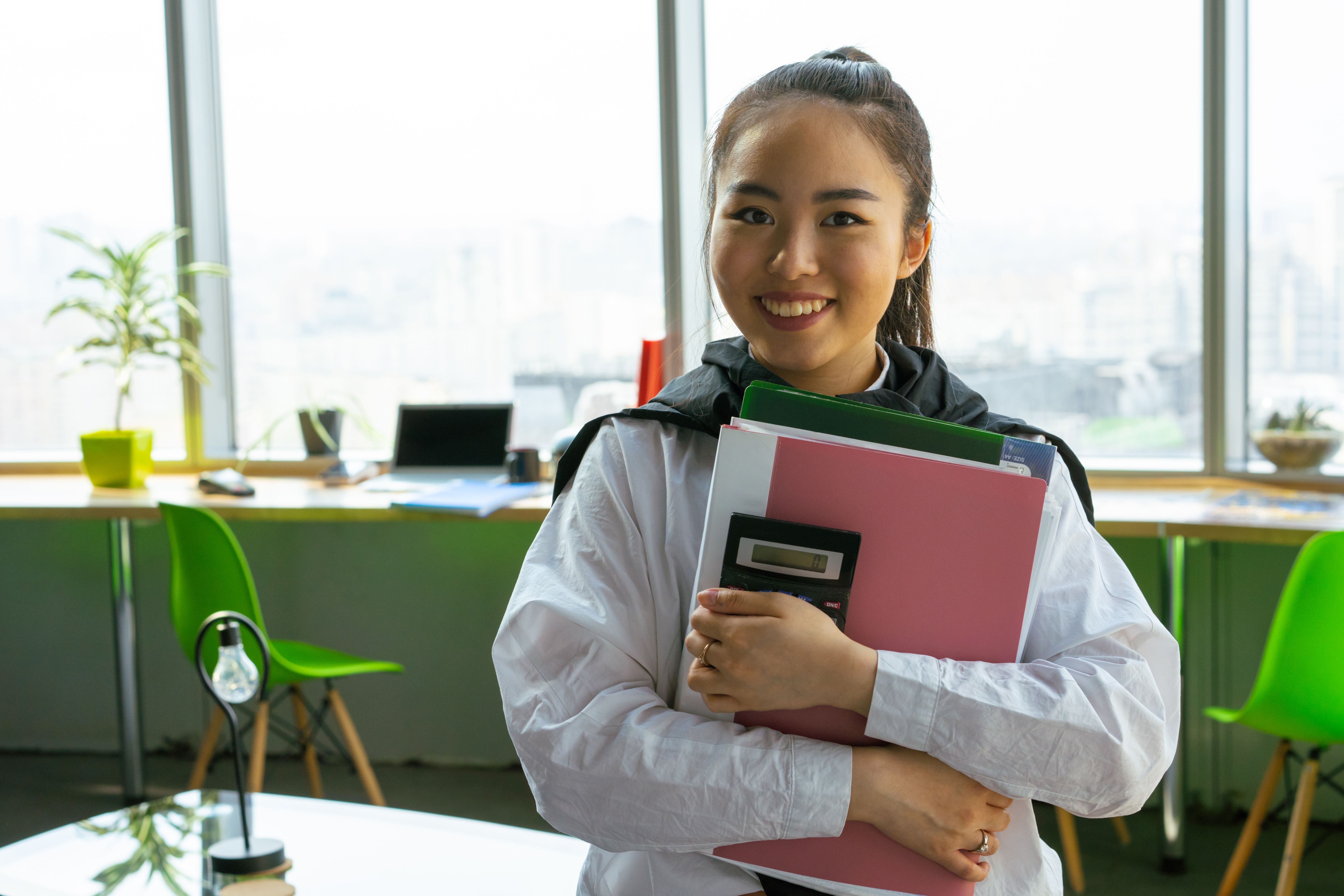 Junge Frau mit Ordnern und Taschenrechner im modernen Büro